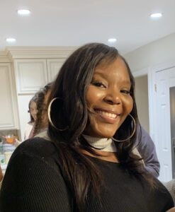A smiling woman with long hair and hoop earrings in a cozy indoor setting.