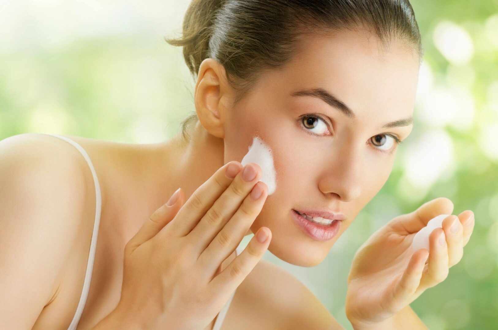 Woman applying skincare cream to her face with a cotton pad.