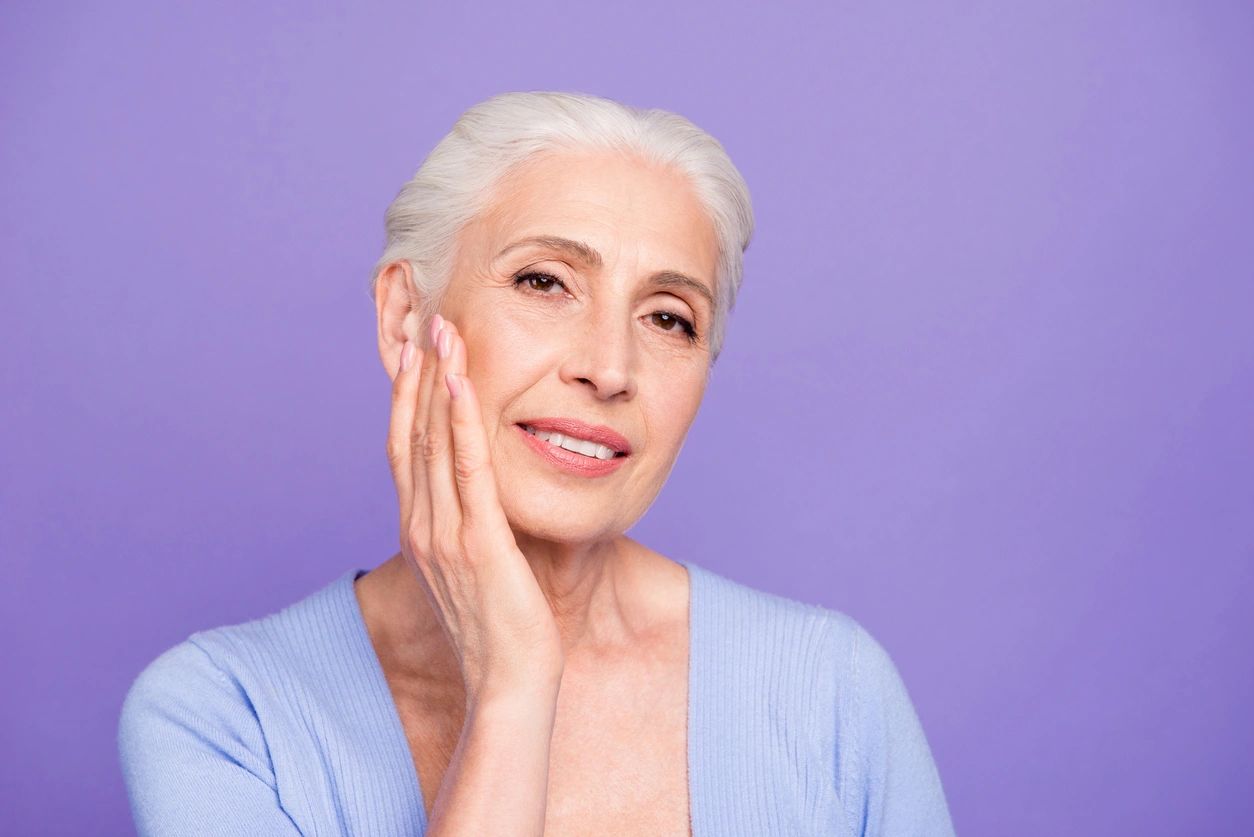 Smiling elderly woman with silver hair against a purple background.