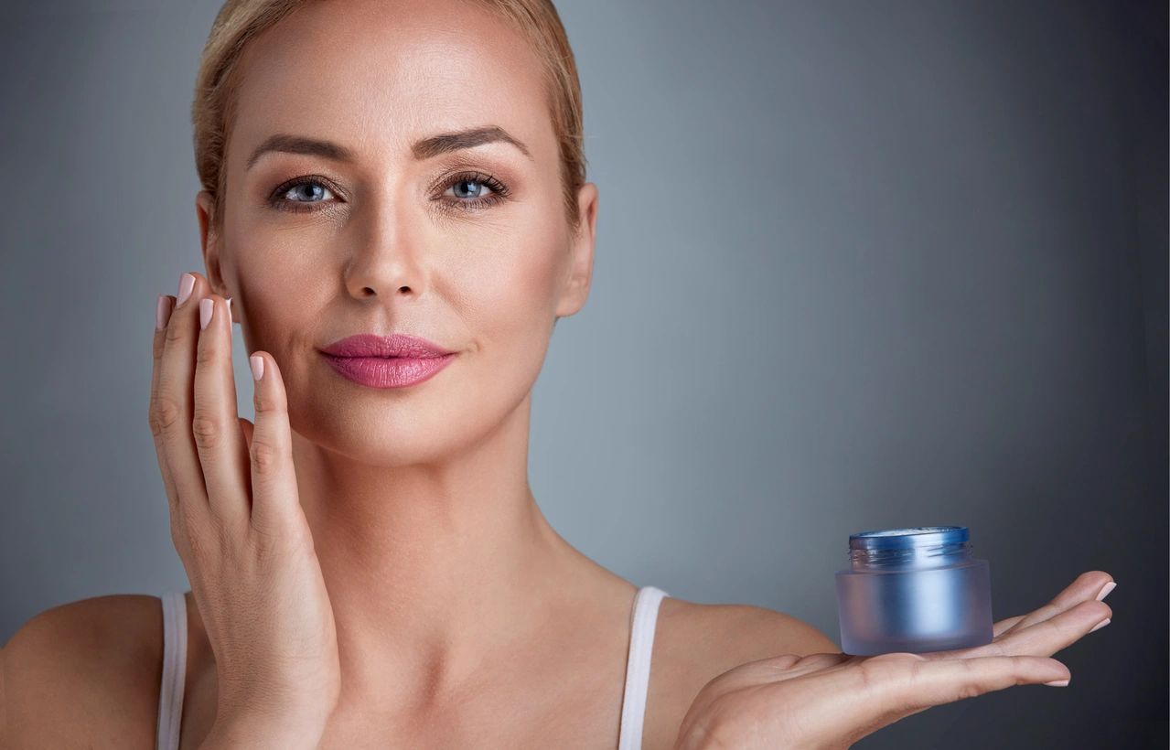 Woman applying moisturizer to her face with a calm expression.