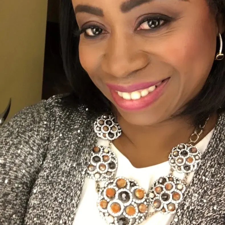 Smiling woman wearing a statement necklace and cozy sweater.