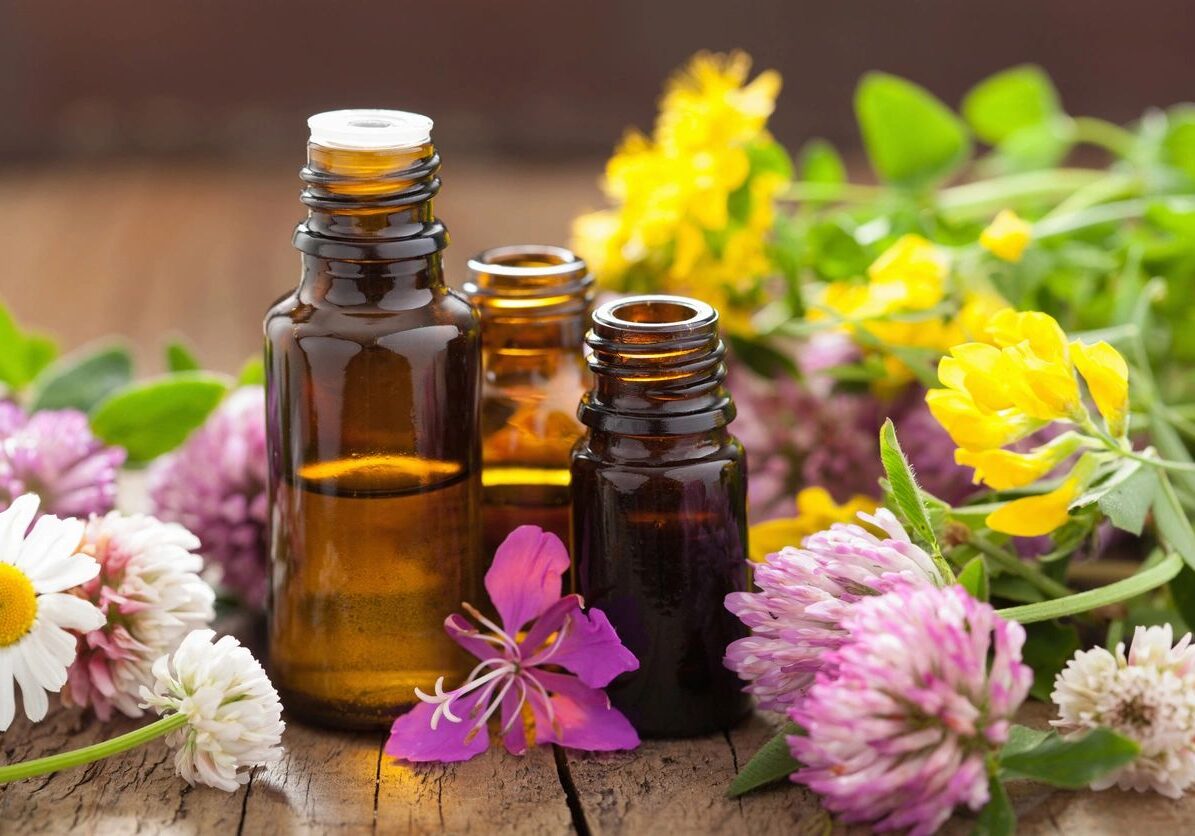 Bottles of essential oils surrounded by colorful flowers.